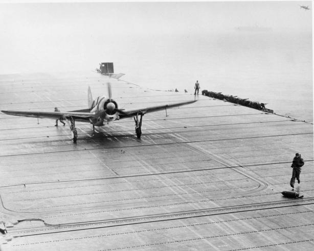 Deck crewman aboard USS Hornet CV-12 disengages tailhook from the arresting gear while another chases stray ordnance that came loose during landing